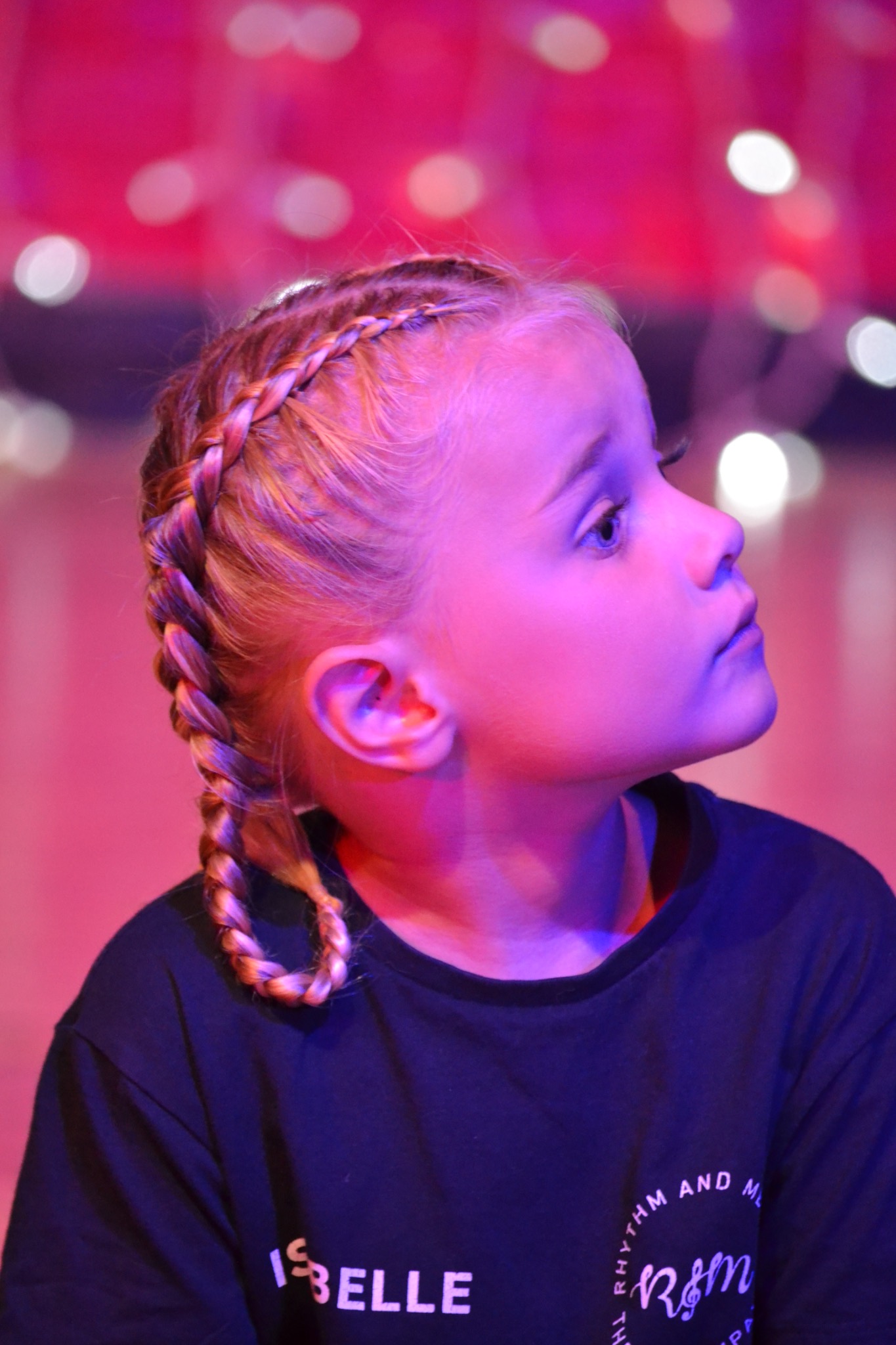 A performer looks towards the side of the stage under colourful lights.