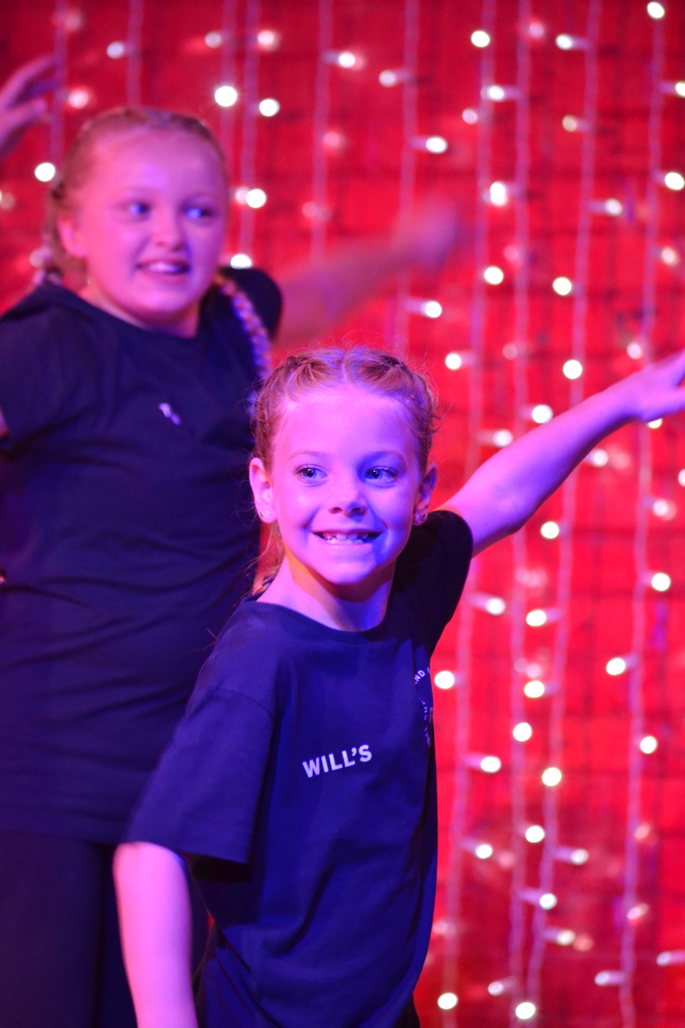 A smiling performer takes part in a dance routine with another performer behind.