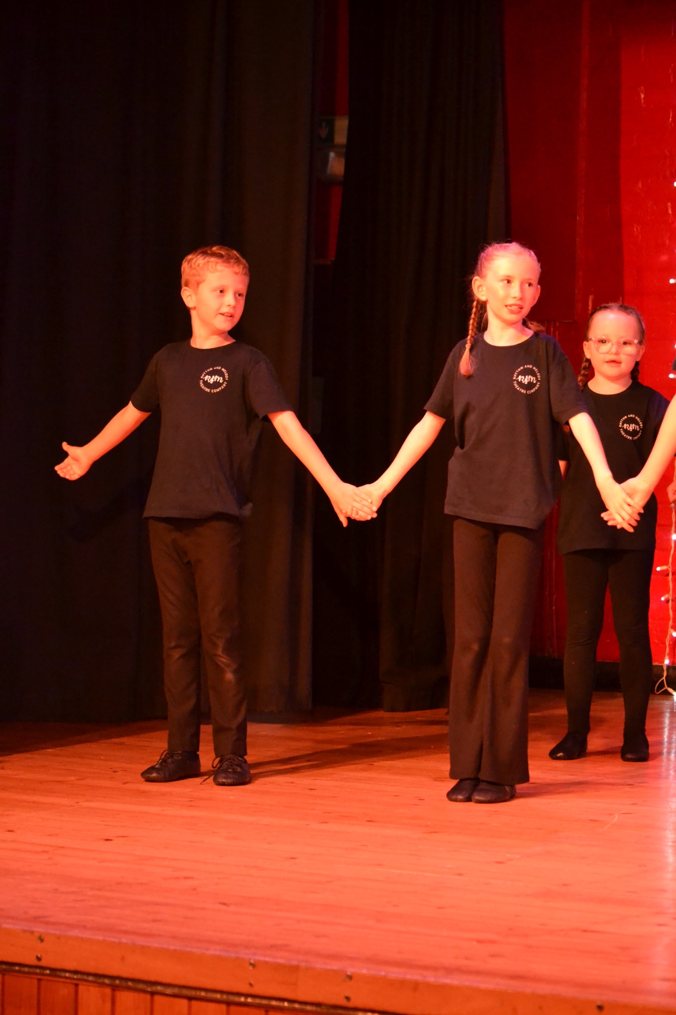 Performers hold hands together on stage in front of a dark curtain.