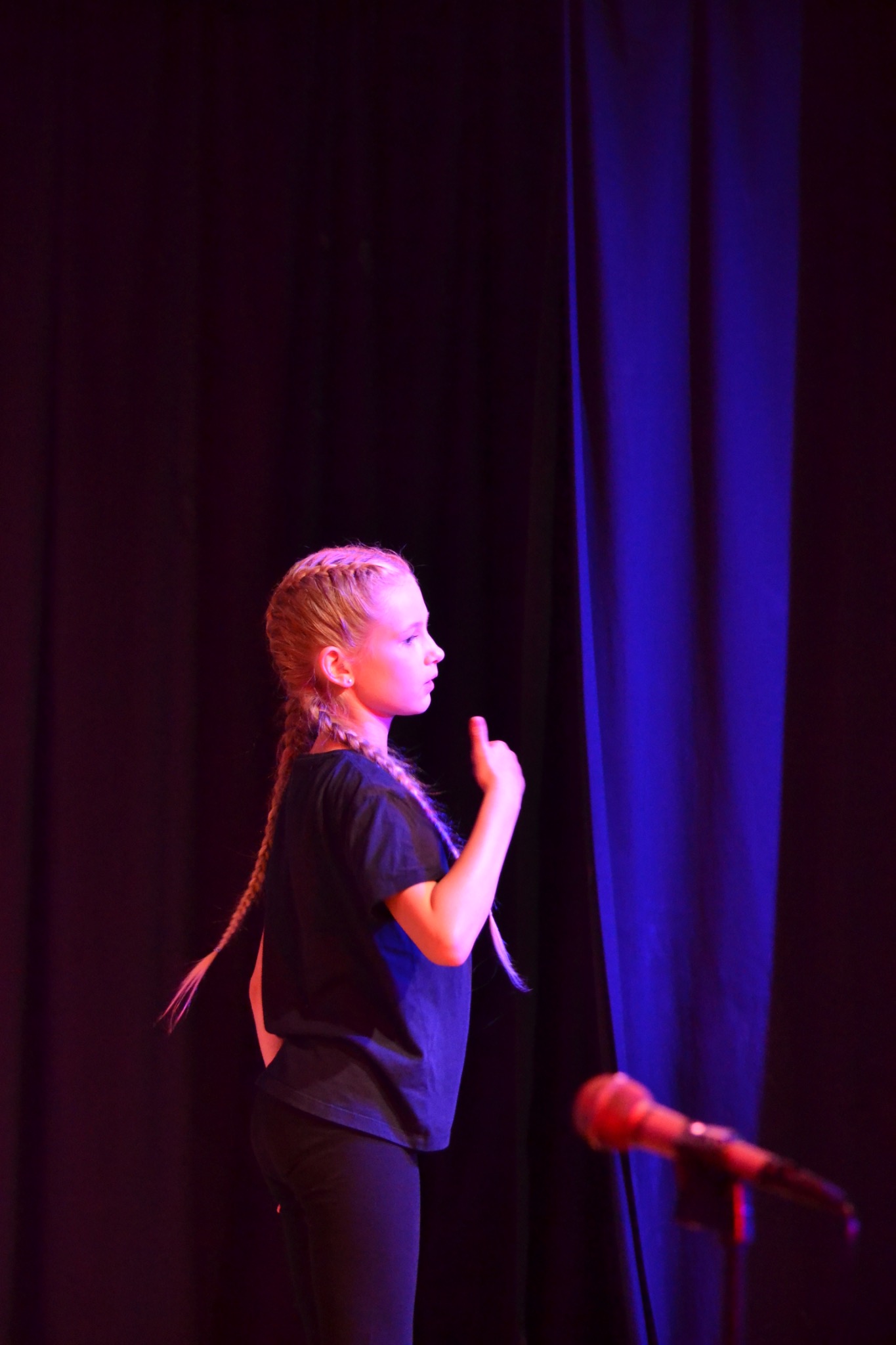 A performer in profile during a routine beside the stage curtain.
